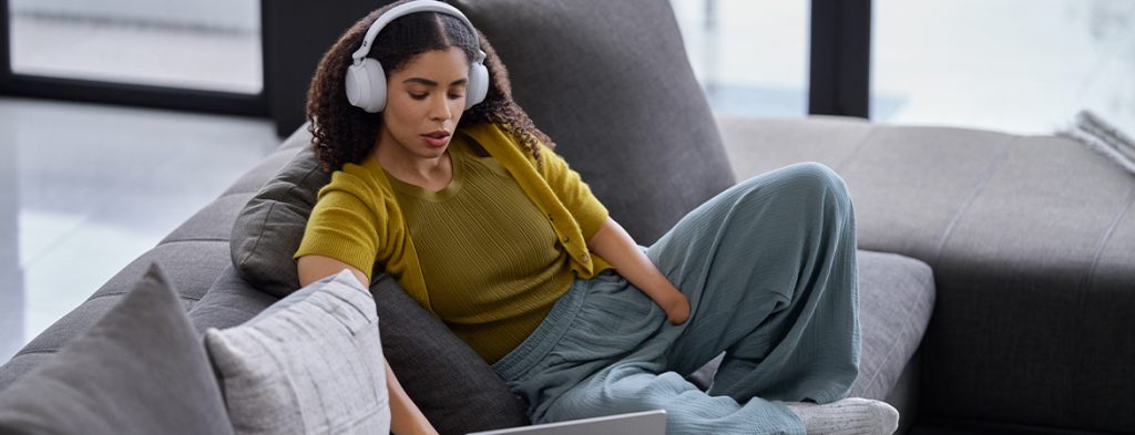 A woman sits on a couch working on a laptop.