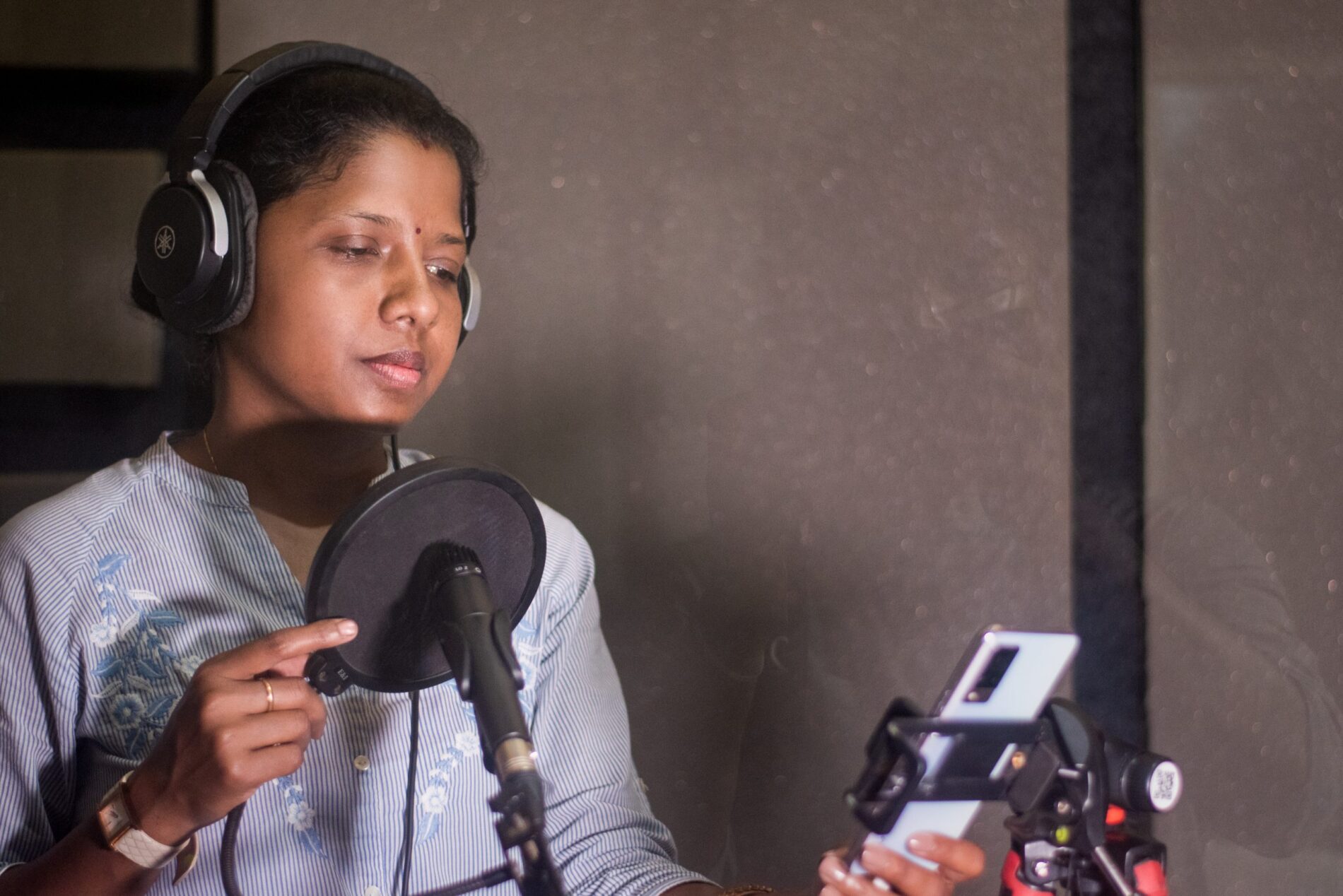 Woman reading from a phone into a mic in a recording studio