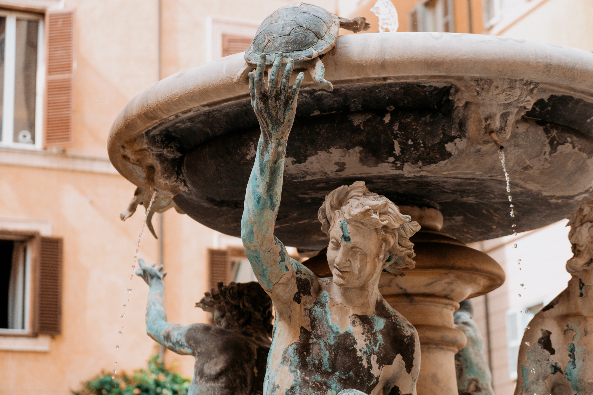 A smiling statue lifts a turtle on a Baroque-style fountain with water flowing from small spouts.