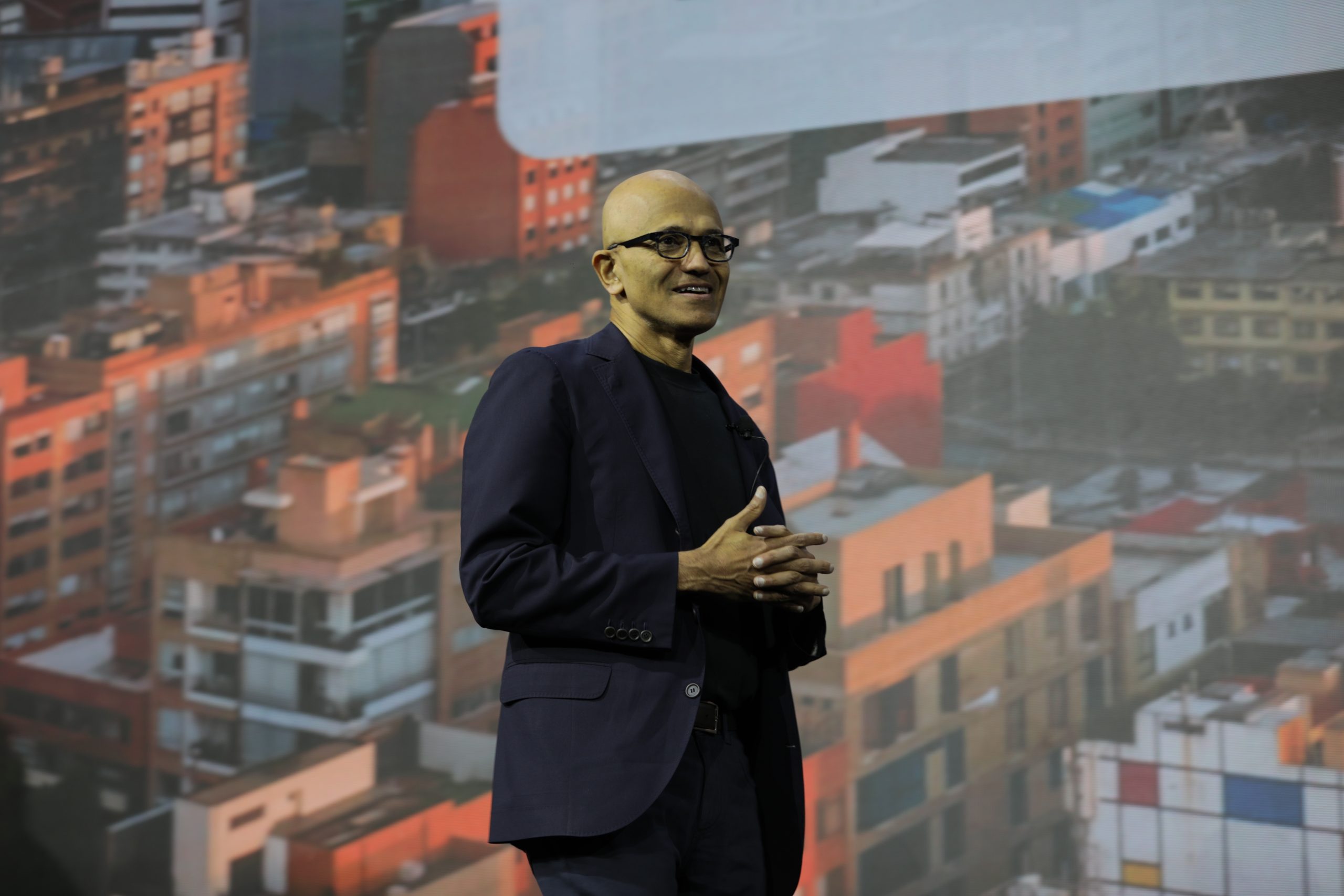 Un hombre de pie en el escenario habla frente a una gran pantalla de proyección