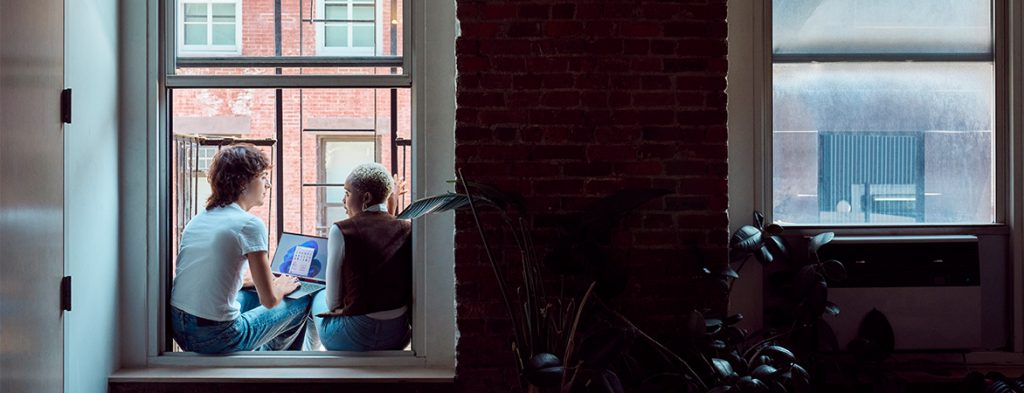 Duas mulheres sentadas no parapeito de uma janela à volta de um computador portátil