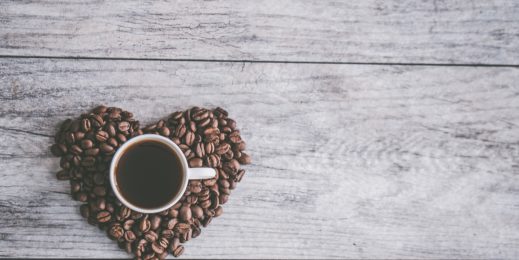 coffee cup on a pile of coffee beans shaped like a heart, on a wooden table